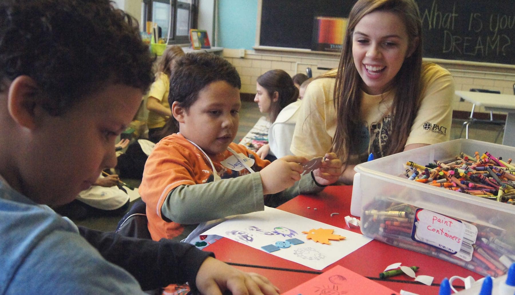 college student at small table helping school children with an art craft