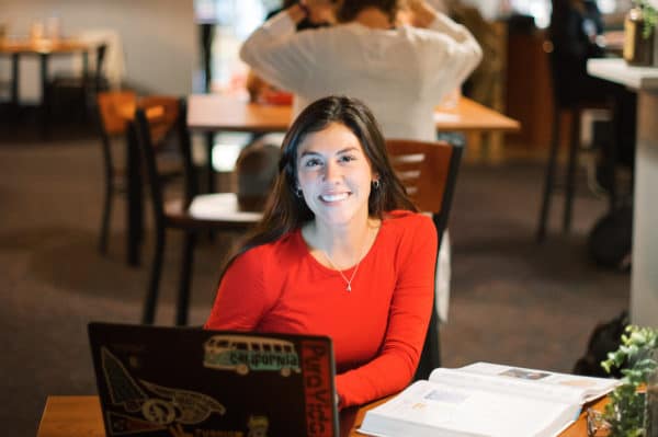 Student smiling and studying with a laptop and textbook at Anderson University. Student smiling and studying with a laptop and textbook at Anderson University.
