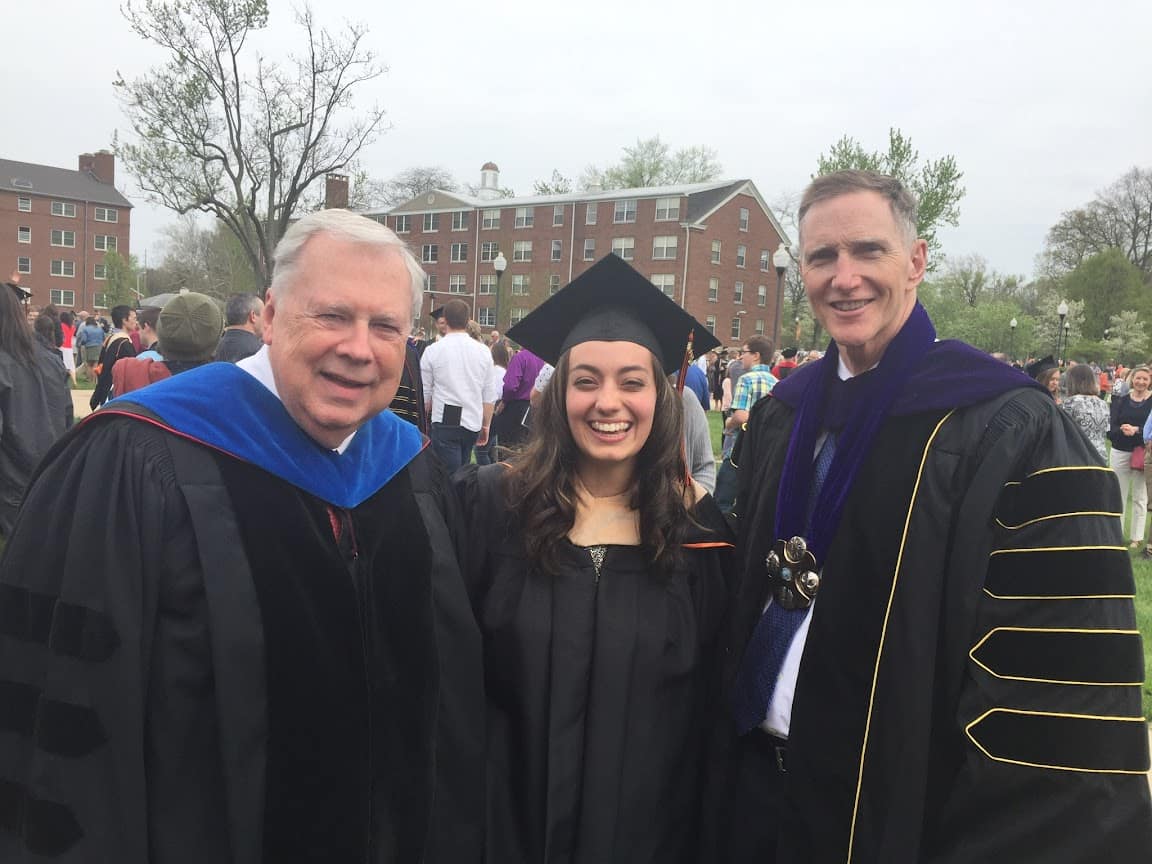 Anna smiles into the camera dressed in a graduation robe, flanked by President Edwards and President Pistole