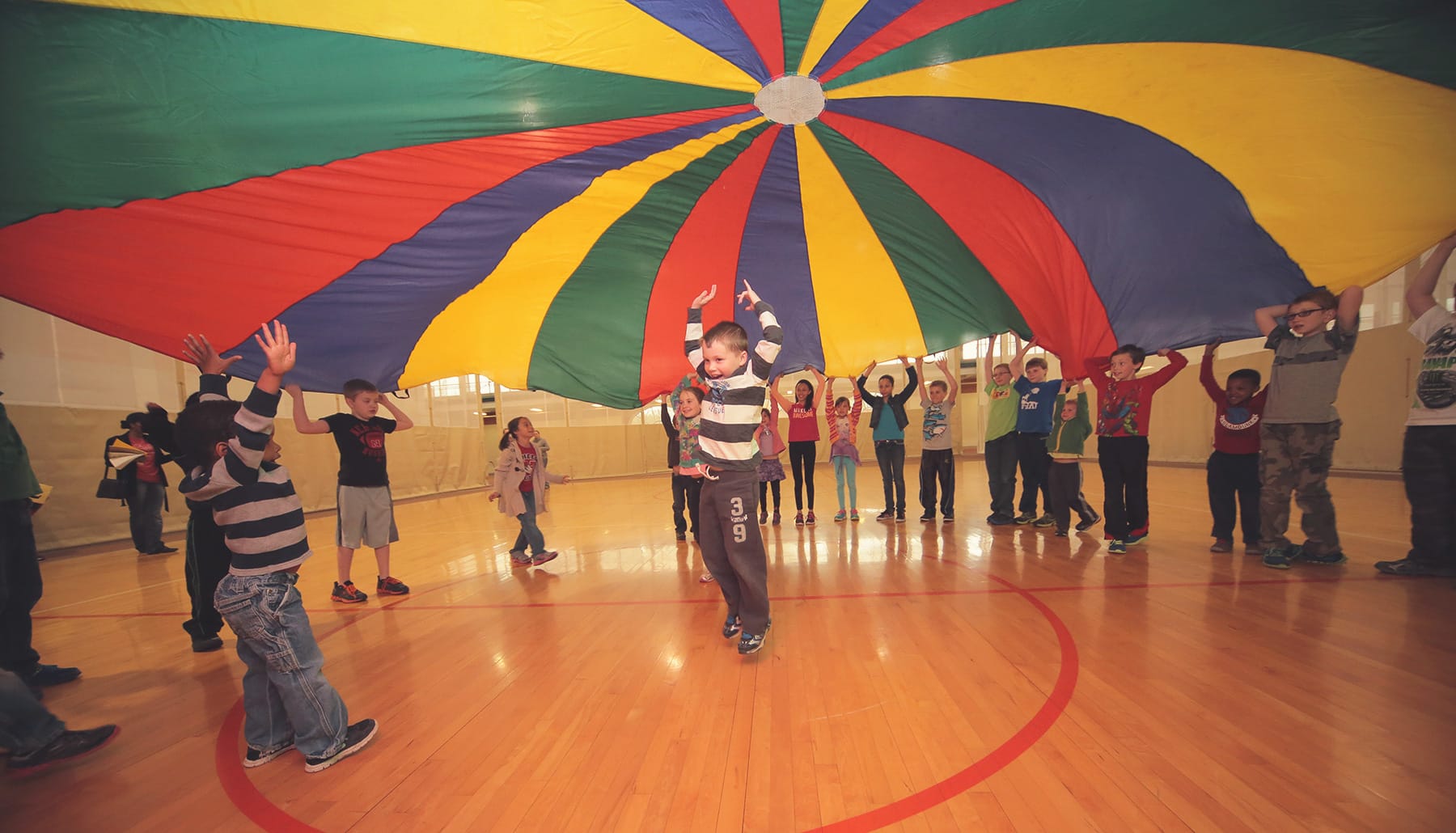 children playing under a parachute on a wooden floor