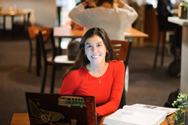 Student smiling and studying with a laptop and textbook at Anderson University.