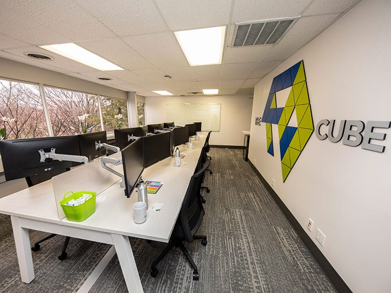 A white room with a blue and green logo on the wall and computers on tables.