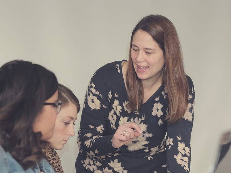 Female professor speaking with two students in class.